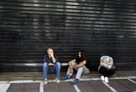יוון, אנשים יושבים מחוץ לבנק סגור / צילום: רויטרס