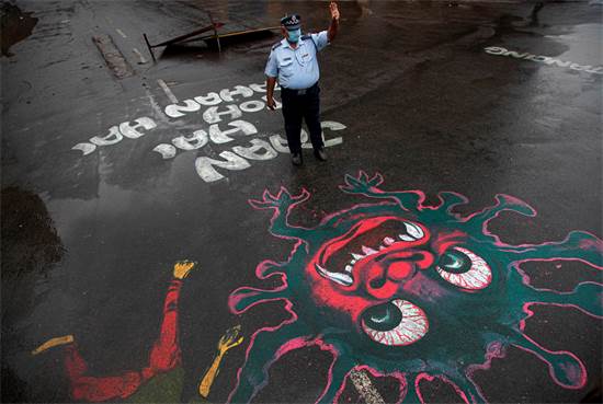 שוטר עומד בכביש שעליו מצויר ציור המעורר מודעות לנגיף הקורונה / צילום: Anupam Nath, AP