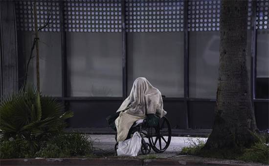 חסר בית יושב על כסא גלגלים בגשם ומנסה לכסות את פניו על מנת לא להידבק בנגיף הקורונה בשדרת סאנסט בלוס אנג'לס / צילום: AP