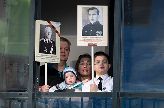 משפחה במוסקבה מציצה מחלון דירתה, מחזיקה בצילומי קרוביה שנלחמו נגד הנאצים, במסגרת ציון יום הניצחון על הנאצים, אמש / צילום: Dmitri Lovetsky, Associated Press