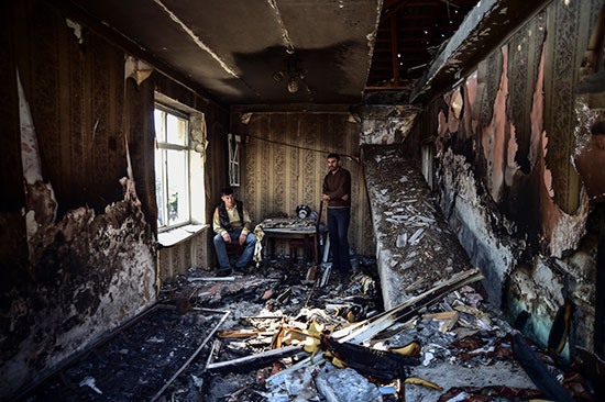 דיירים יושבים בקצה דירתם שנהרסה כליל בעיר טרטר, אזרבייג'ן. רק שרידים של השטיחים נשארו לאחר ההפצצות  / צילום: Ismail Coskun, Associated Press