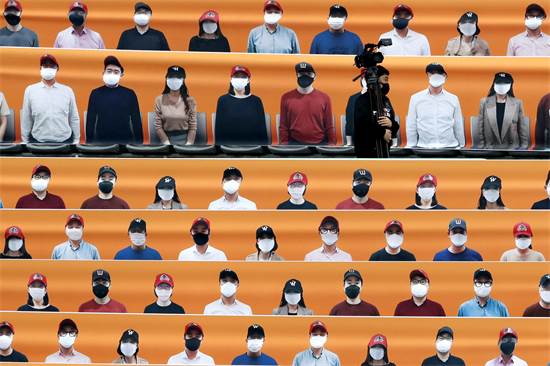 צלם עובר דרך יציע שמכוסה בצילומים של אוהדים לפני פתיחת משחק בייסבול בדרום קוריאה. משחקי הליגה חודשו ב-5 במאי, אך נאסר לשחק עם קהל / צילום: Lee Jin-man, AP