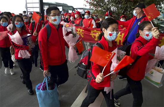 עובדים רפואיים ממחוז ג'ילין בסין מנופפים בדגלים סיניים כשהם מתכוננים לחזור הביתה בשדה התעופה הבינלאומי ווהאן / צילום: AP