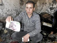 קרוב משפחה של התינוק עלי דוואבשה מציג את תמונתו בזירת הרצח / צילום: רויטרס