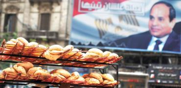 אדם נושא כיכרות לחם בקהיר על רקע שלט תעמולה בעד הנשיא סיסי /  צילום: רויטרס