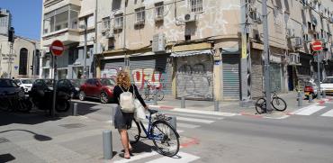 צעירה עם אופניים משקיפה על הרחוב הריק, דרום תל אביב. מאז התפשטות הקורונה משרד הבריאות הורה על סגירת מרבית העסקים במדינה / צילום: איל יצהר, גלובס