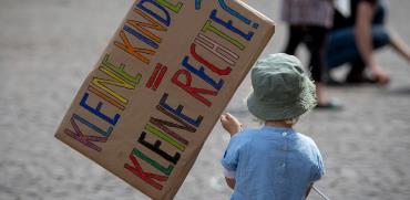פעוטה מחזיקה שלט במסגרת מחאת הורים על התייחסות המדינה לזכויות ילדים קטנים בתקופת הקורונה / צילום: Michael Probst, Associated Press