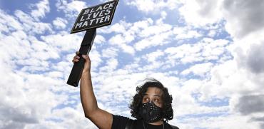 מפגין מחזיק שלט שנושא את המילים שמהדהדות את המחאה על רצח ג'ורג' פלויד / צילום: Associated Press