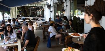 מלצרית מגישה מנות לסועדים בבית קפה בתל אביב / צילום: Sebastian Scheiner, Associated Press
