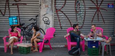 צעירים יושבים מחוץ לבית קפה שנפרס לרחוב על רקע העסקים הסגורים בשעת יום / צילום: כדיה לוי, גלובס