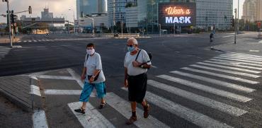 עוברי אורח עם מסכות עוברים שלט על מגדלי עזריאלי שאומר לחבוש מסכה / צילום: Oded Balilty, Associated Press