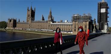 אנשים עם מסכות הולכים על רקע בניין הפרלמנט הבריטי בלונדון / צילום: Kirsty Wigglesworth, AP