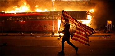 מפגין נושא את דגל ארה"ב הפוך ליד בניין בוער במינאפוליס, העיר שבה נרצח ג'ורג פלויד / צילום: Julio Cortez, AP