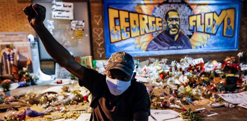 מפגין עומד על רקע קיר זכרון לנרצח פלויד ג'ורג' / צילום: John Minchillo, Associated Press