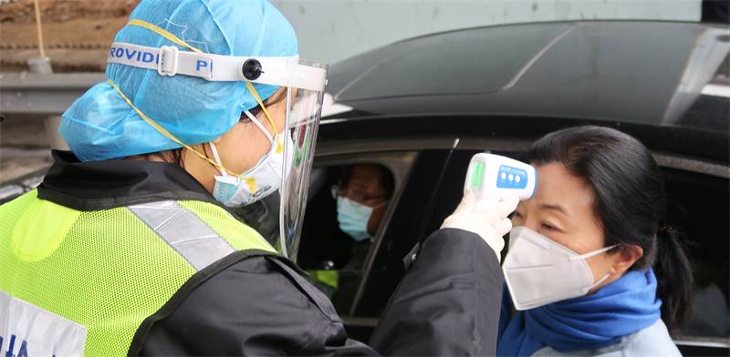 איש ביטחון בכביש אגרה בסין בודק את חום גופה של נוסעת, כדי לשלול הידבקות בנגיף קורונה / צילום: Martin Pollard, רויטרס