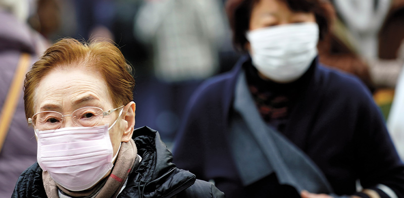 אישה מבוגרת הולכת עם מסכה בתוך קהל של אנשים / צילום: Eugene Hoshiko, Associated Press